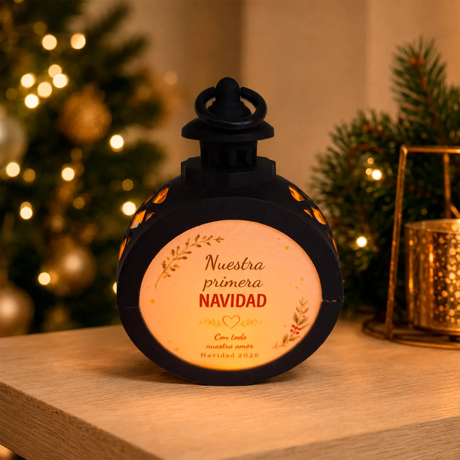 Farolillo LED redondo negro personalizado con el diseño «Nuestra primera Navidad», dedicatoria y fecha, encendido en un ambiente navideño.